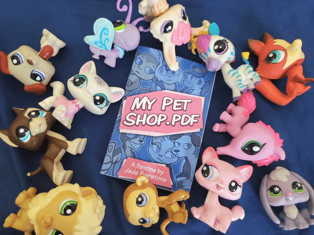 a bunch of littlest pet shop figures surrounding a booklet version of the zine