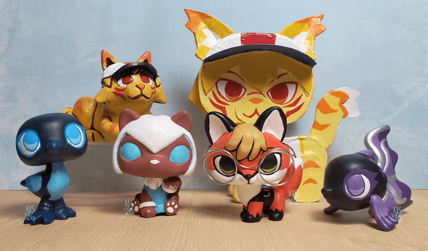 from left to right, a blue and black magpie LPS, a polymer clay figure of a cat version of nix, a cat version of TRAN, An lps version of Xenia the linux fox, A cardboard cat of Nix, and a black and purple fish LPS